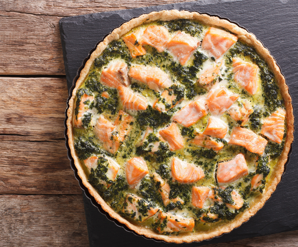 Tasty Savory Tart with salmon and spinach in the dish for baking close-up on the table. vertical view from above