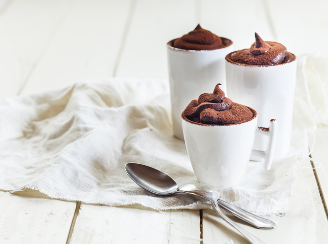 Three cups of vegan mousse au chocolat, tea spoons, cloth on white wood